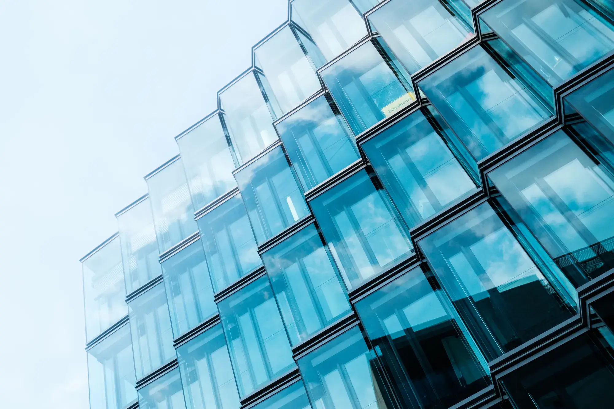 Angular glass office facade with faceted bay windows reflecting clouds and sky