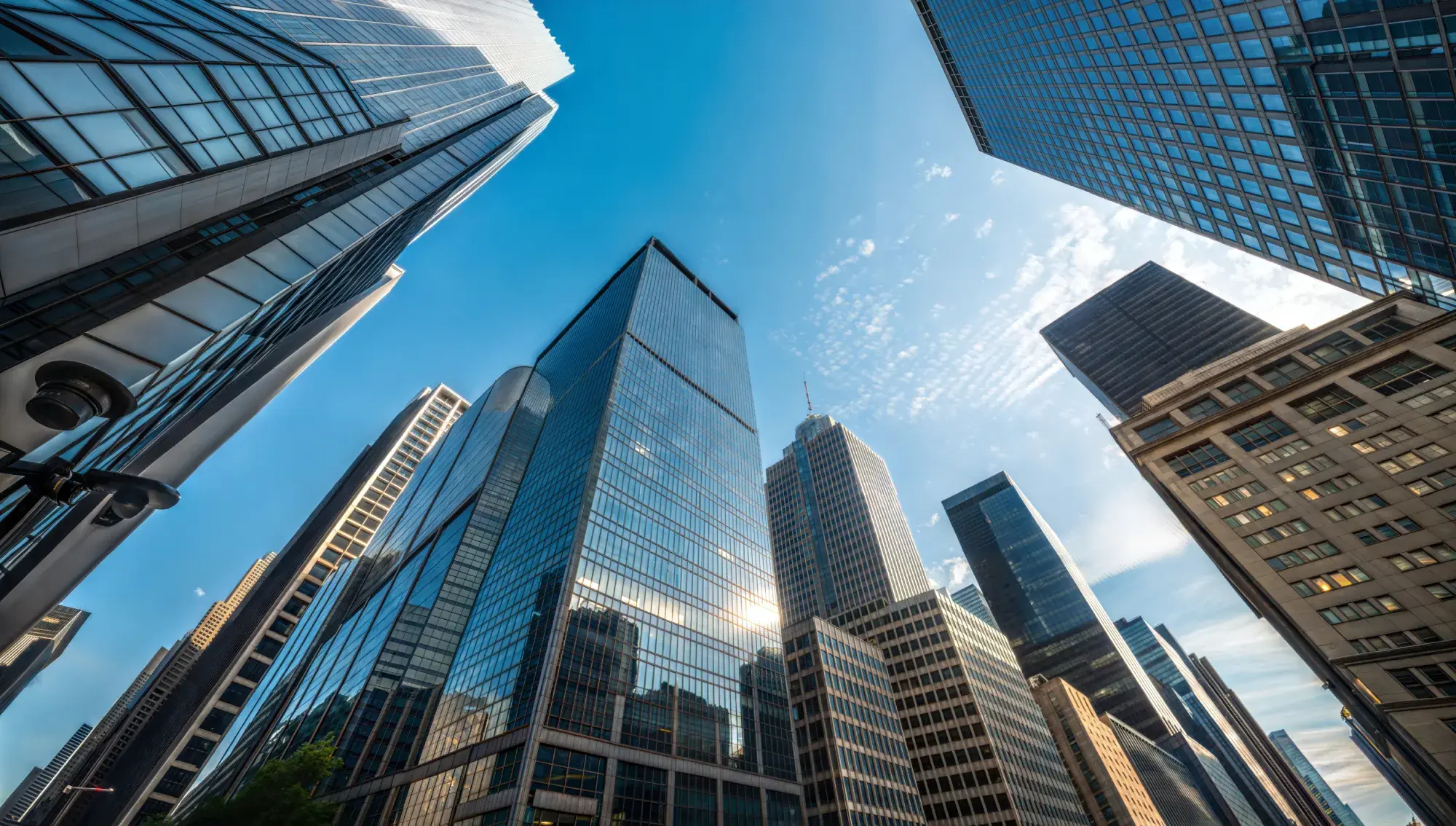 Upward view of dense downtown skyscrapers reflecting a bright blue sky